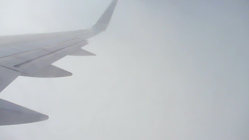 Flying through clouds in airplane looking out from window seat.