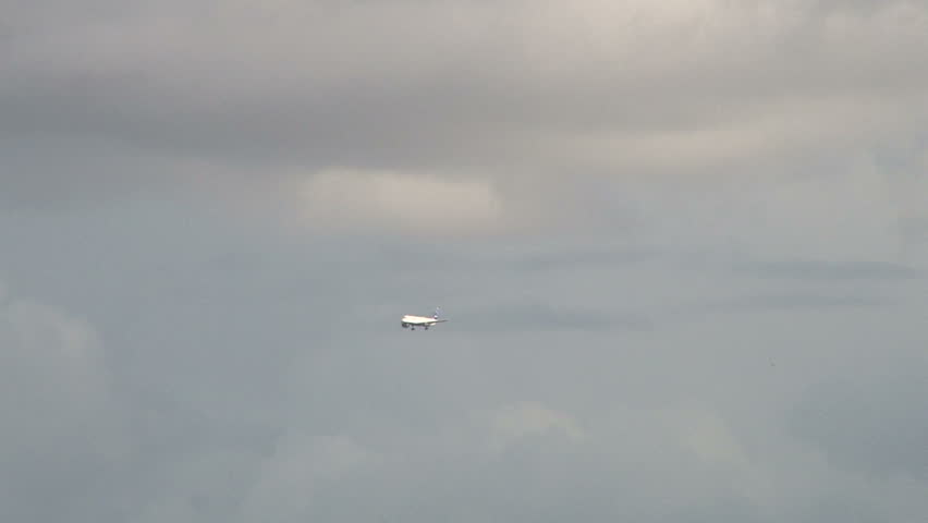 Airplane flying low under clouds with landing gear out, wide shot.