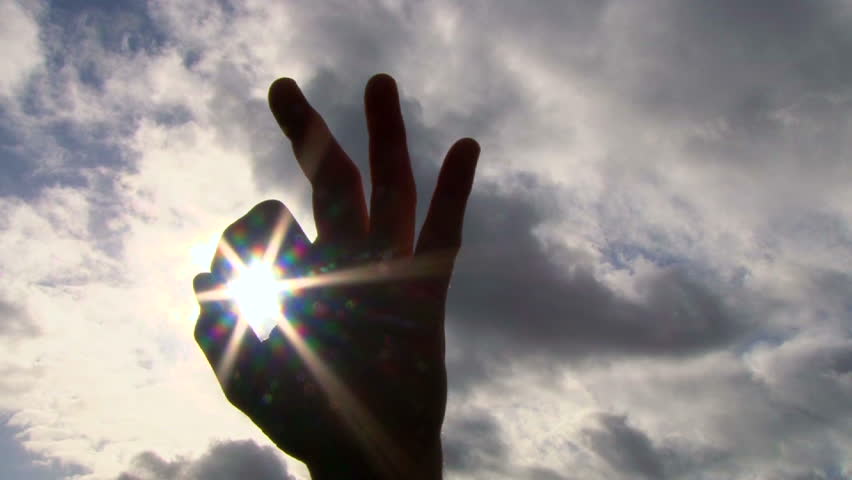 Hand rising into frame to give an a-okay sign with sun shining through then