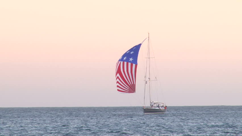Sailboat mid sea lowers its main sail designed as an American Flag. Shot near