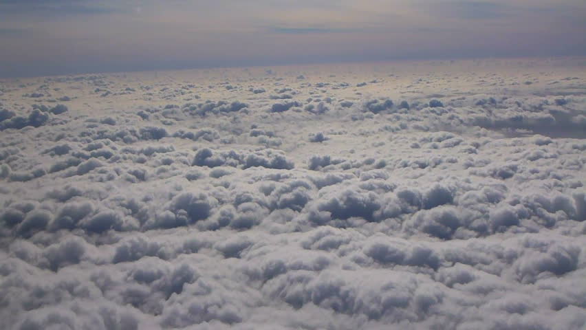 Flying in airplane over clouds on hazy and sunny day.