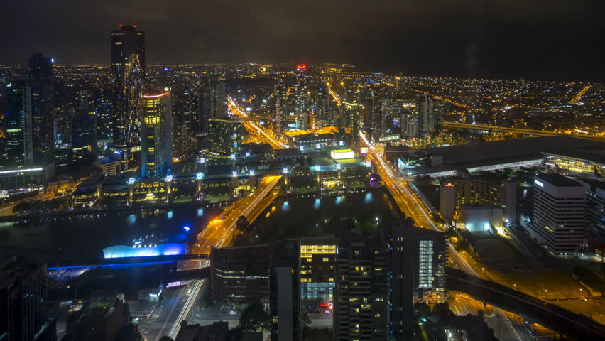 An aerial view of Melbourne cityscape including Yarra River and Victoria Harbour in the distance. 4k Time lapse during night time with light trail from traffic. tilt up