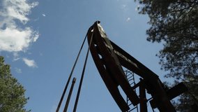 An anonymous and well used oil donkey pumping out oil from the forest in Mississippi on a hot and sunny day. There are ten clips from different angles in this series. 