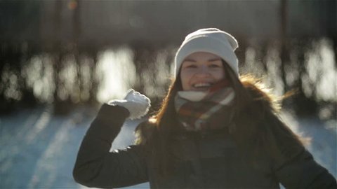 Smiling Girl Enjoying Cold Sunny Morning in the Park. Cheery Active Woman is Throwing Snowball at the Camera Having Fun Outdoors during Winter Time.