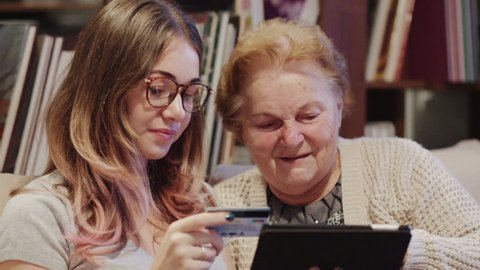 Young Woman Helping Her Grandmother For Using A Digital Tablet and credit card
