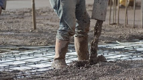 Close up, Slow Motion. Construction worker controls the concrete flow while another vibrates the concrete mix. Before concrete can be poured, forms need to be built to hold the concrete in place
