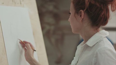 Young woman drawing in pencil using easel and explaining the process