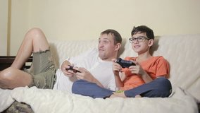 father and son play video game inside their house on the couch