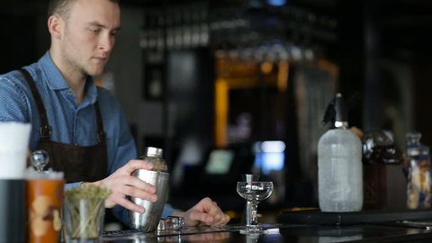 Young bartender communicates with the customer and prepares a cocktail for him