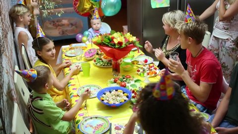 Three women and five children sit at the banquet table and celebrate birthday