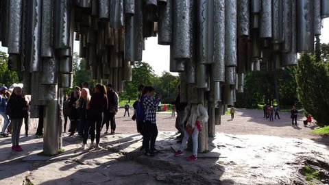 HELSINKI, FINLAND - SEPTEMBER 09, 2016: Group of unidentified school children examine Sibelius Monument, curious girl stand with head inside steel pipe. Camera tilt up and down, girls take pictures