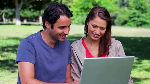 Smiling couple using a laptop together in a parkland