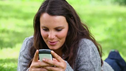 Smiling brunette woman sending a text message in a park