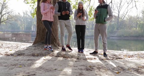 Young People Group Using Smart Phone Outdoor Sunrise, Two Couple Network Communication Morning Autumn Park Near Tree Natural Sun Lights Slow Motion 60