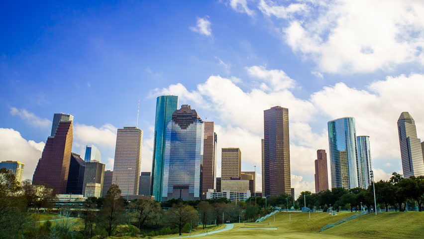 Houston Texas Clouds Time Lapse 4K 1080p. A time-lapse of Houston skyline with clouds rolling over buildings and blue skies. Shot from a park with grass and trees