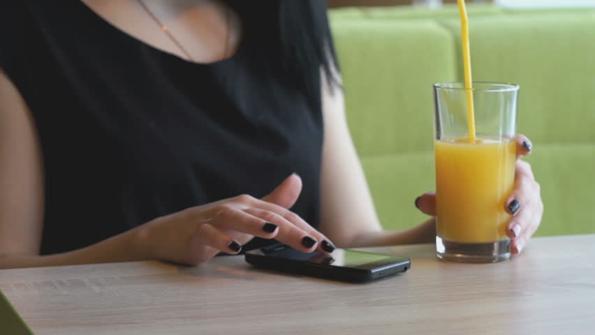 Stylish student girl aged 20s viewing photos using a black smartphone at the restaurant