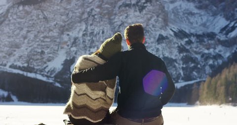 A girl rests and relaxes watching snowy mountains in front of them embraced with boyfriend, lovers embrace after the walk in the snow. Concept: the mountains, relaxation, hiking, love