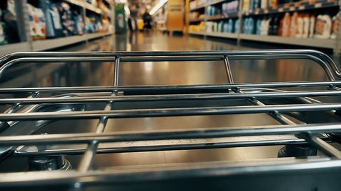 Big supermarket shopping cart in motion goes between blurred shelves. Color graded