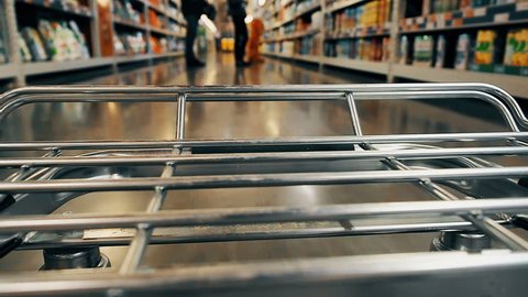 Accelerated timelapse video of big supermarket shopping cart in motion goes between blurred shelves. Color graded