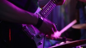 Guitarist plays an electric guitar in close-up on stage. A musical group performs in a nightclub