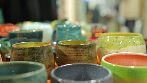 Lady choosing decorative handmade pottery bowls at ceramic store, shopping. Woman holding local souvenirs, searching for present, exhibition sale, art. Female shopaholic buying traditional plates
