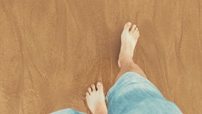 Point of view looking down at male legs with rolled up jeans and bare feet walking near ocean