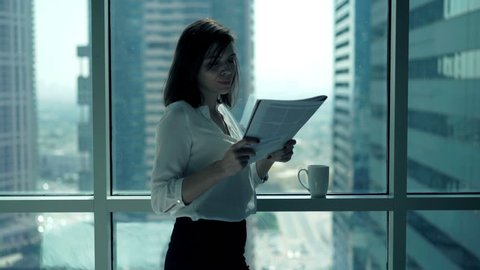Young businesswoman reading newspaper standing by window in office
