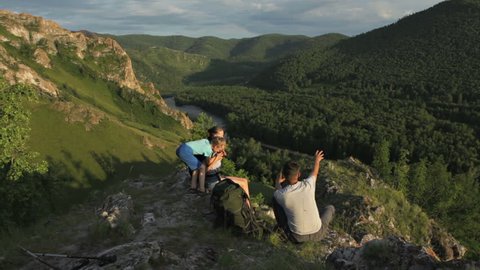 Backpacker family of three people sitting and having enjoy of beautiful nature view in a rock mountains in a summer day. Camera moving by slider.