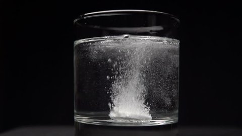 Effervescent Antacid Tablet in Glass of Water on Black