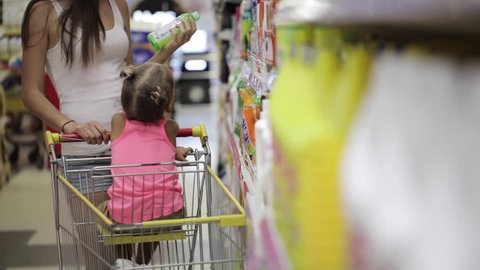 Young women with cute little daughter selecting detergents for house at supermarket