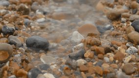 Very shallow stream of water flowing downstream over small pebbles and stones.