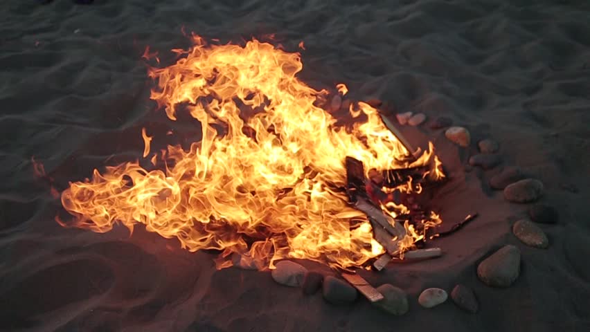 Fire crackles inide a stone circle on the beach sand. (Santiago, Chile - Feb 2016)
