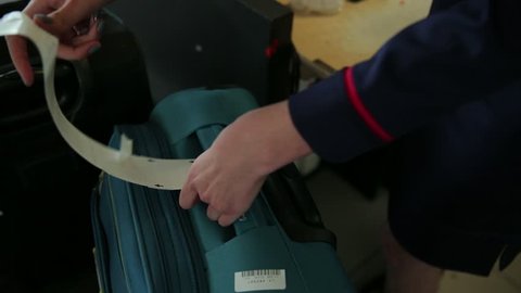 Close-up of female hands placing baggage-claim ticket around suitcase handle. (Santiago, Chile - Jun 2016)
