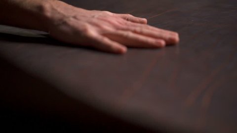 A craftsman sleeking a big piece of leather on the table slow motion