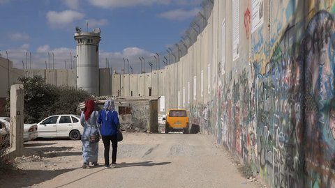 BETHLEHEM, WEST BANK - OCTOBER 2016: Veiled Palestinian women walk past the separation barrier between the West Bank (Bethlehem) and Israel
