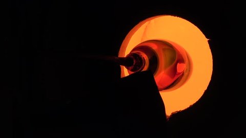 Glassblower also known as gaffer blowing glass heating the glowing hot vase in oven furnace turning the rod with glass to keep it round and smooth located at a glassmith glass and crystal workshop 4k