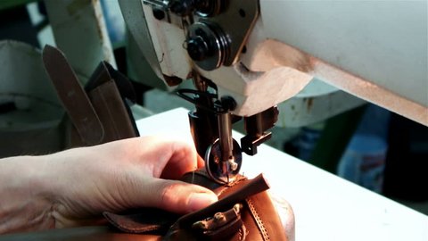 Worker sews leather for shoe production with sewing machine