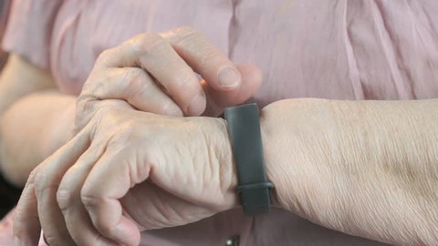 Wristband of heart rate monitor. The elderly woman touches and looks at the wristband of pulse monitor indoors
