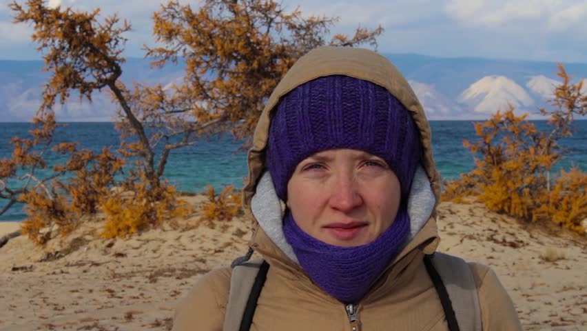 Portrait of a girl in a jacket with a hood standing on the shore of the sea