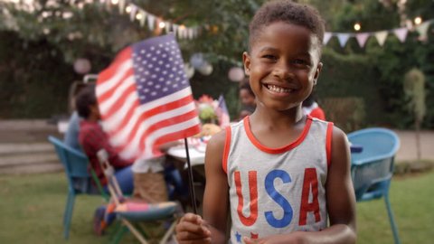 Young black boy waving US flag at 4th July family barbecue