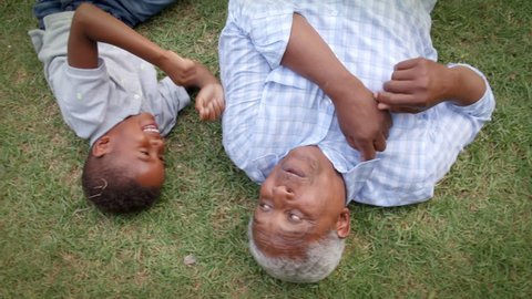 Black grandad and grandson play lying on grass, aerial view