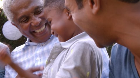 Young black boy playing with dad, uncle and grandad outdoors