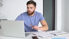 Young concentrated man working with laptop and blueprints at home 