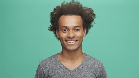 Young afro american man showing negative and positive human emotions isolated on the green background