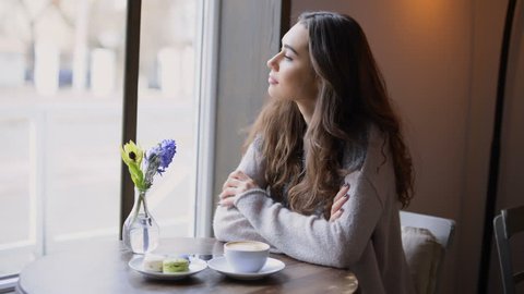 Beautiful young woman looking at the window and drinking coffee in cafe
