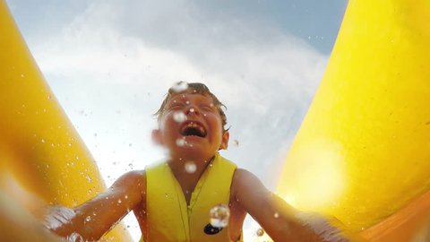 4K Video: Little boy slides fast by the inflatable slide into the water pool with active camera in front of his face