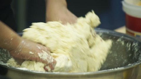 cooker kneads dough with both hands in bowl in industrial kitchen