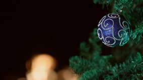  this is a holiday video of a blue ornament hanging from a Christmas tree. The background is black allowing space for text and copy. There is a slow motion fire in the background out of focus.
