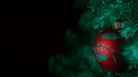 This is a holiday video of a red ornament hanging from a Christmas tree. The background is black allowing space for text and copy. There are no people in this video.
