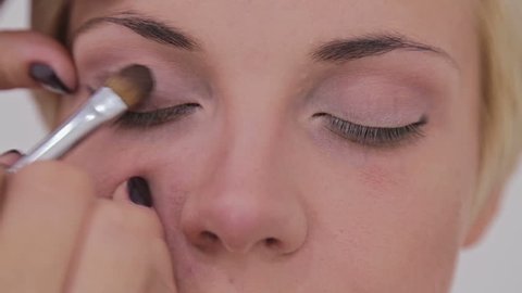 Professional make-up artist applies eye shadow to eyelid of model in white room. Beauty, makeup and fashion concept